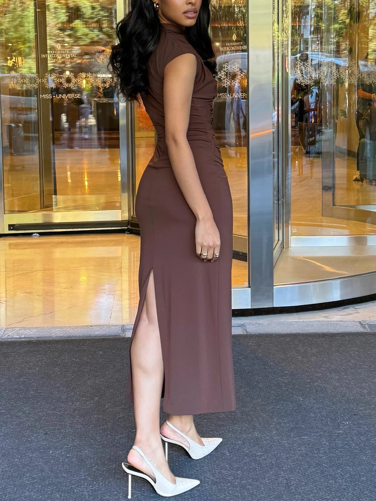 Woman in a brown dress standing in front of a glass door.