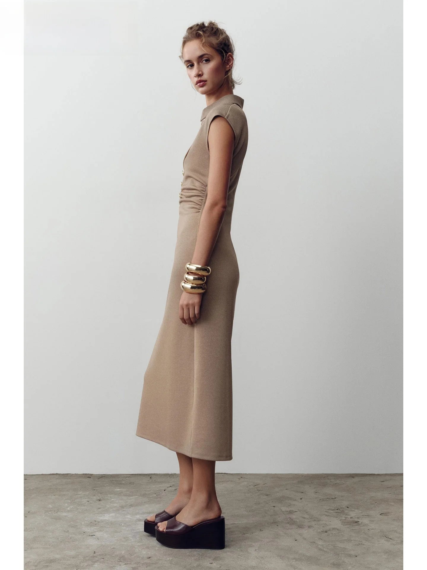 Woman wearing a beige dress with gold bracelets against a white background